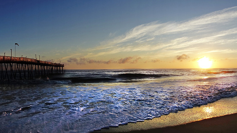 The sun rising over the ocean beside Avalon Pier with waves rolling onto the sand.