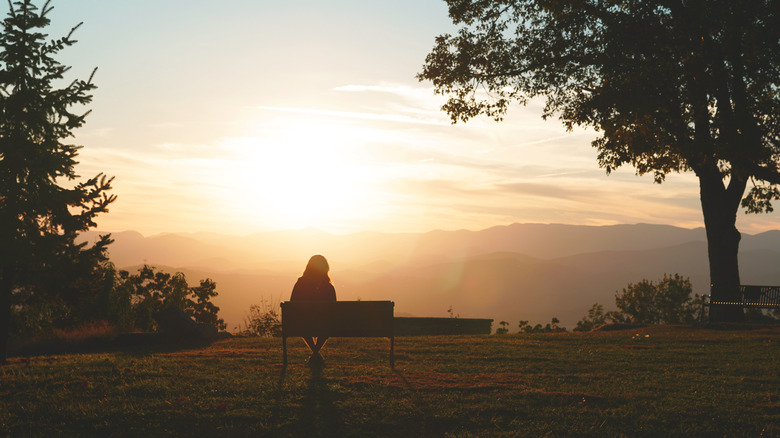 A woman sitting on a bench watching the sunrise over mountains at Jump Off Rock