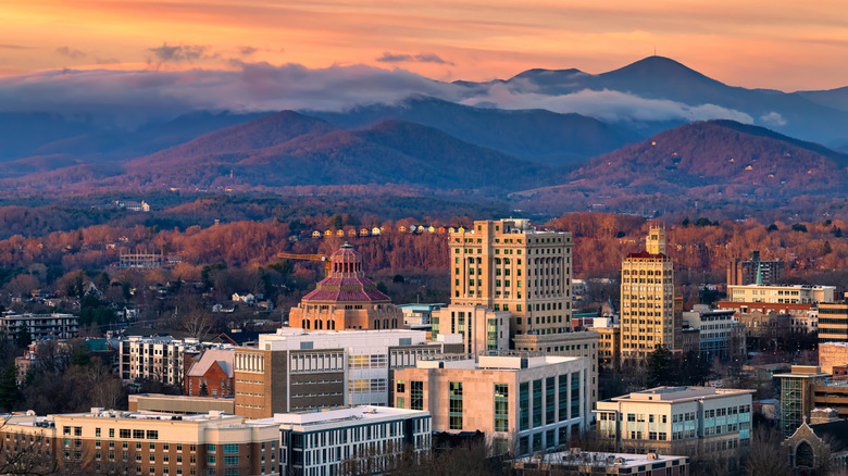 Downtown Asheville skyline against a backdrop of mountains and fall foliage at sunset
