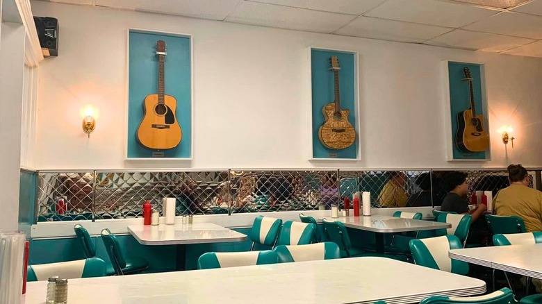 Retro-style interior of Oscar's Restaurant in Roanoke Rapids, North Carolina, with teal diner chairs, white tables, and framed guitars on the wall