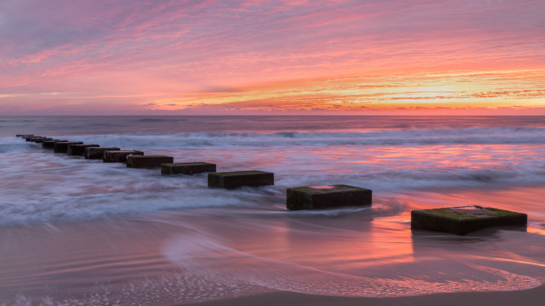 Concrete pier remnants extending into the ocean at sunset