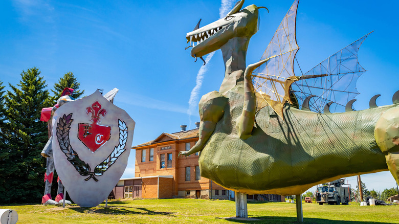 A sculpture of a green dragon with wings and a red knight sculpture with a shield under a blue sky