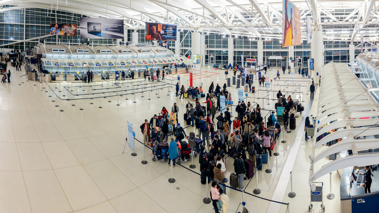 An overhead shot shows a crowd of travelers queuing in front of airline service desks at John F. Kennedy Airport in New York