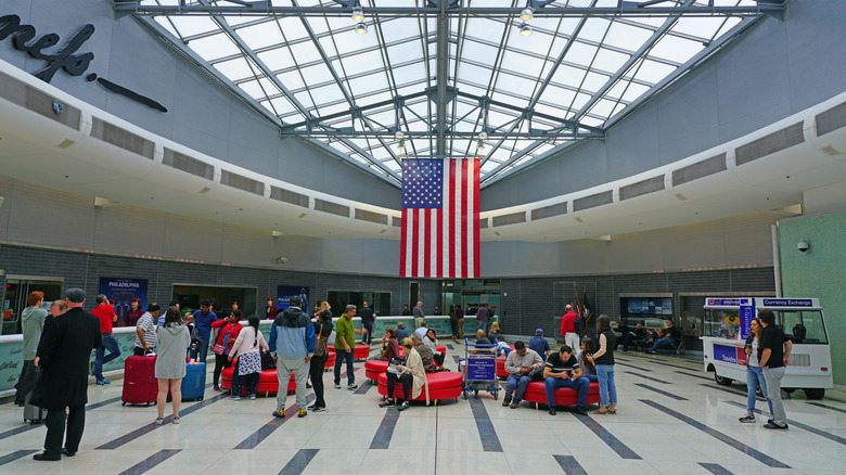 Travelers gather around colorful sofas beneath an American flag in Philadelphia International Airport