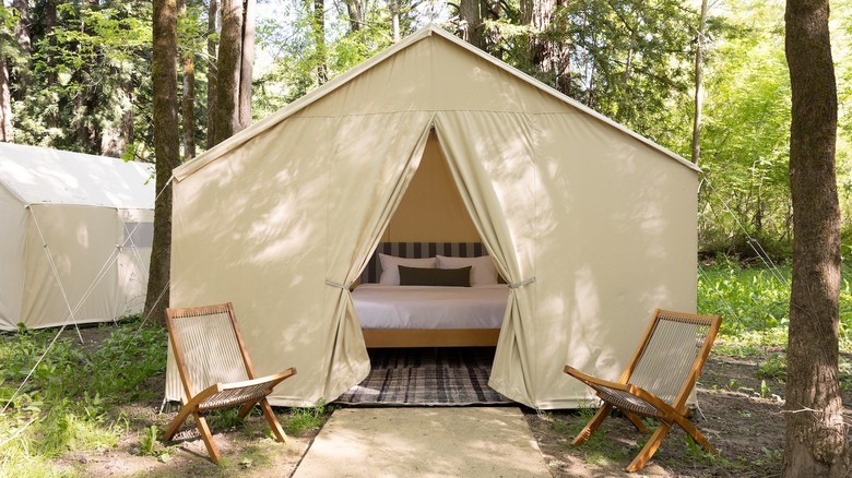 A refined canvas tent framed by wooden lawn chairs hides luxury bedding within