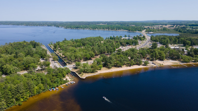 An aerial photo over Lake Mitchell showing the canal connecting to Lake Cadillac with green trees and a road sliding through
