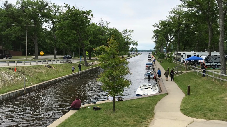 The canal connecting Lake Mitchell and Lake Cadillac with boats tied up on one side, campers nearby, and lots of leafy trees