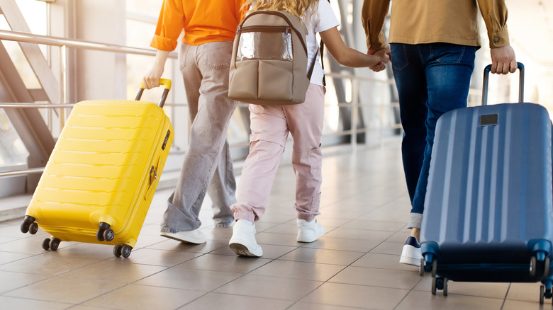 A family walking together at airport holding hands and dragging luggage