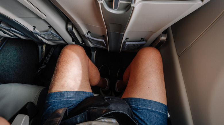 An airplane passenger's legs with cramped legroom.