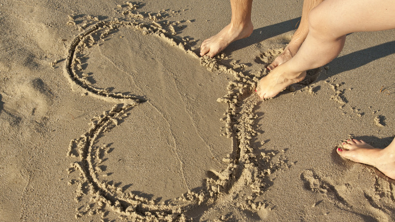 Drawing heart in sand on beach
