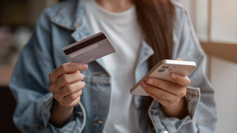 A woman holding a credit card and a cell phone