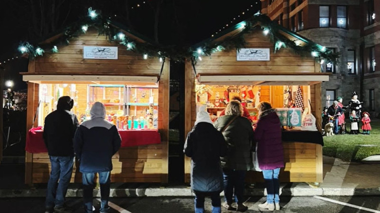 Wooden vendor stalls at Bryan, Ohio's Christkindlmarkt, with a brick building and carolers in the background under a night sky