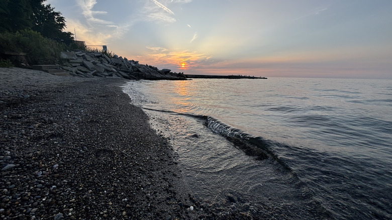 The sun setting over Lake Erie with a rocky beach at Geneva Lake State Park.