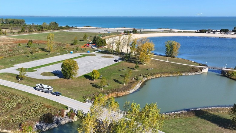 A view of Maumee Bay State Park with a sandy beach in the background and an RV towing a car on the road in the foreground.
