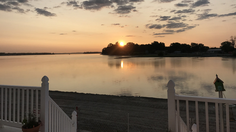 White fence overlooking lake with sunset and trees in backgorund