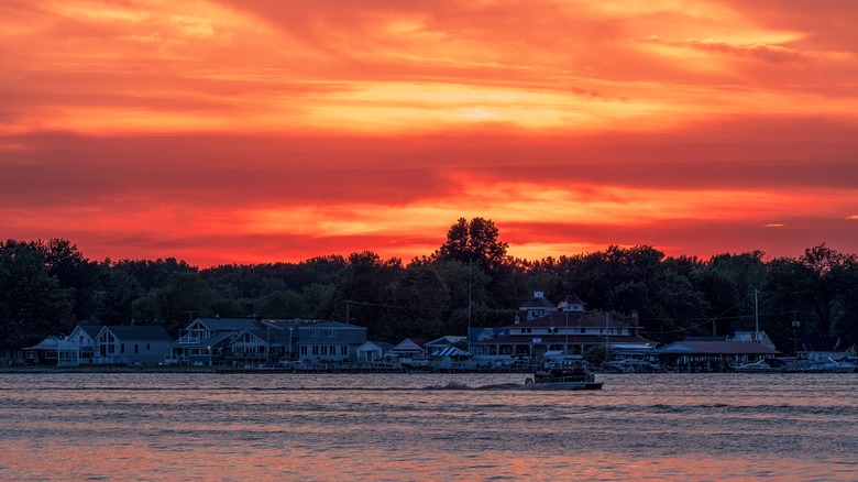 Water with a boat on it and orange sunset behind it