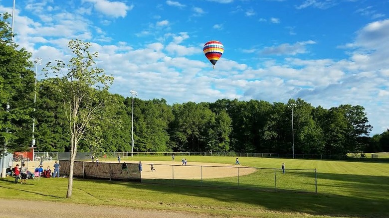 A colorful hot air balloon above the trees and a baseball diamond in Ohio