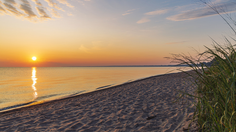 A sunset over Lake Erie with the beach in the foreground and some grass in the right corner.