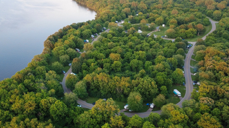 Campsites at Buck Creek State Park, with RVs along a road looping through green trees and the lake in the upper left of the frame
