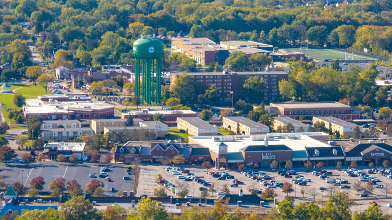 Aerial view of Strongsville, Ohio, with a green water tower surrounded by buildings, a shopping center in the foreground, and a football field and trees in the background