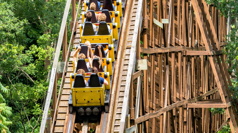People riding a wooden rollercoaster between green trees