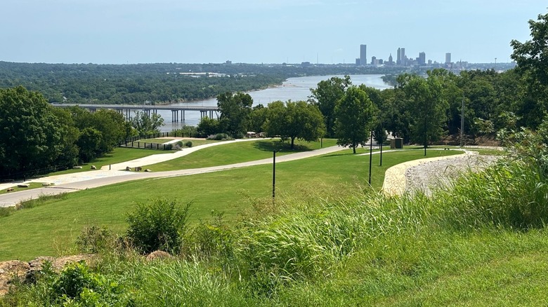 Grassy hills with trees and walking paths at Chandler Park overlooking the water and Tulsa city skyline in Oklahoma