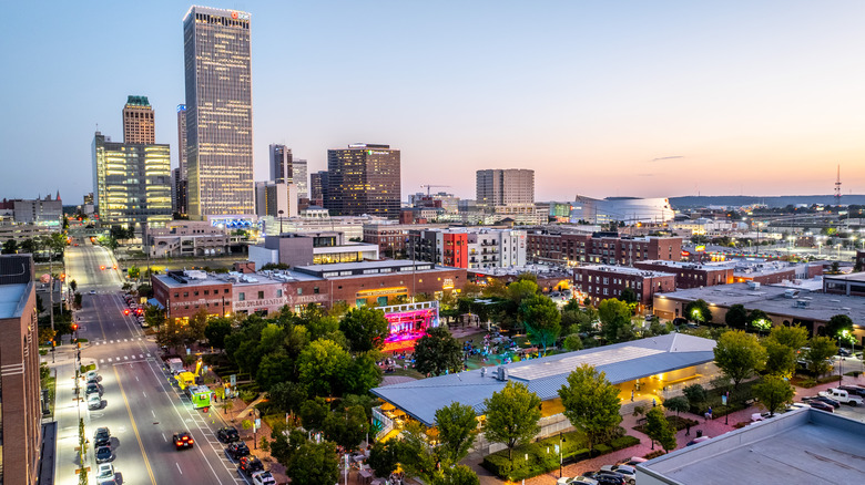 Aerial view of Guthrie Green park lit up for an outdoor concert at dusk with Tulsa, Oklahoma's city skyline in the background