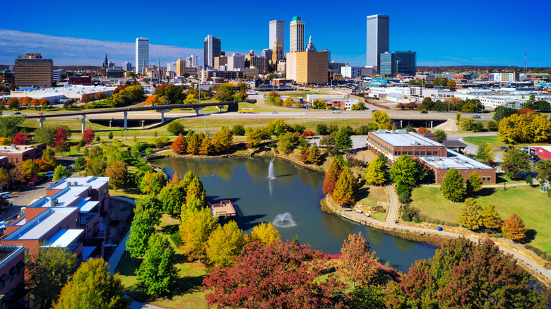 Wide aerial shot of Tulsa, Oklahoma city skyline in the distance with parks and a lake in the foreground