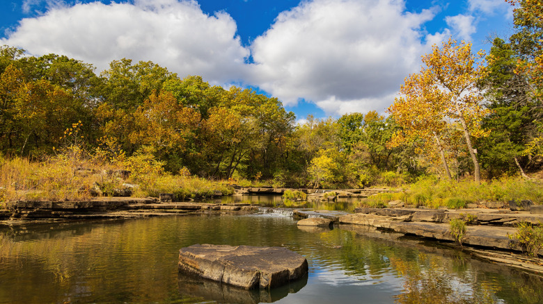 Blue sky and clouds over a rocky lake surrounded by trees within Oklahoma's Osage Hills State Park