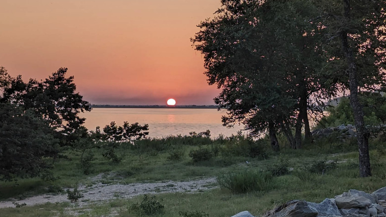 A wide shot of the sunset over Lake Eufaula taken from a patch of grass with trees around