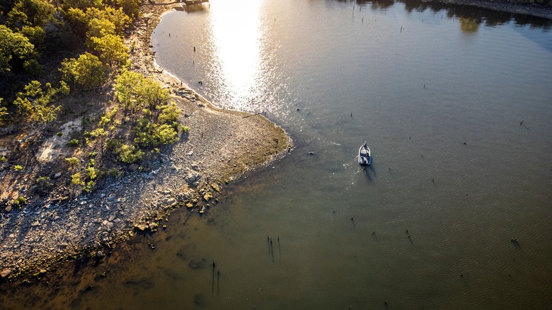 Aerial shot of fishing boat near muddy Lake Eufaula shoreline