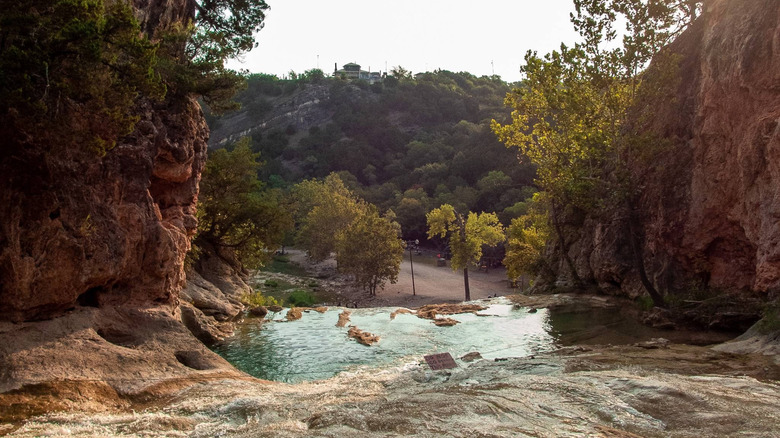 A pool of water set between two rocky outcrops with trees and a road in the background