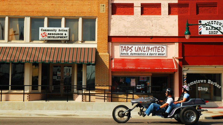 Two men on a motorbike on the road passing businesses in historic downtown Claremore, Oklahoma.