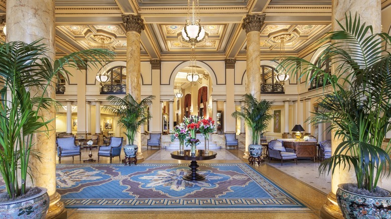 Lobby of The Willard InterContinental, with marble floors and columns, white-accented yellow walls, armchairs, and potted plants under hanging lights