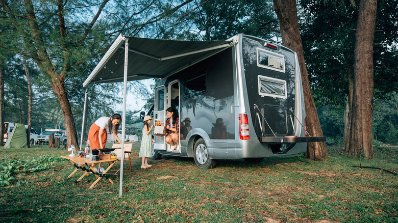 A family enjoying RV camping in the woods besides a reservoir