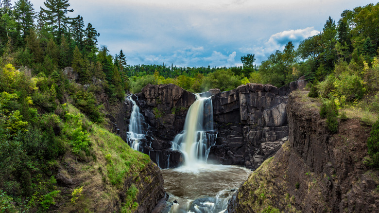 The High Falls at Pigeon River Provincial Park falling down the stone cliff into the river below with green forest all around