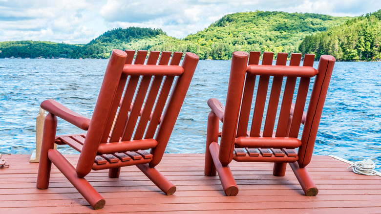 Two red wooden chairs on a dock overlooking a lake