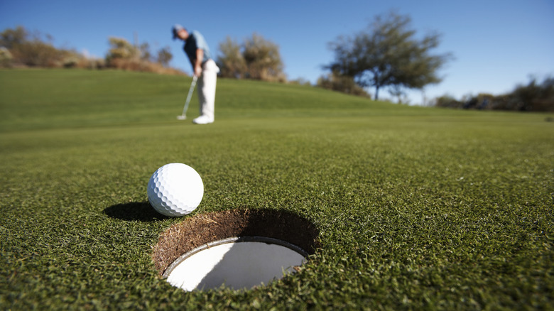 Golf ball near hole with golfer in the background