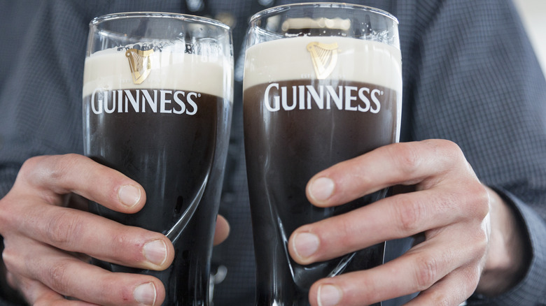 A person holding two pints of Guinness beer