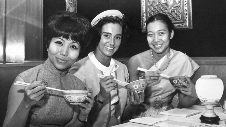 TWA air hostesses from Vietnam, Hong Kong, and France in uniform holding up bowls of food