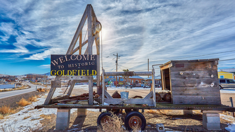 Welcome to Historic Goldfield sign onold wooden trailer with highway and wispy clouds in the background