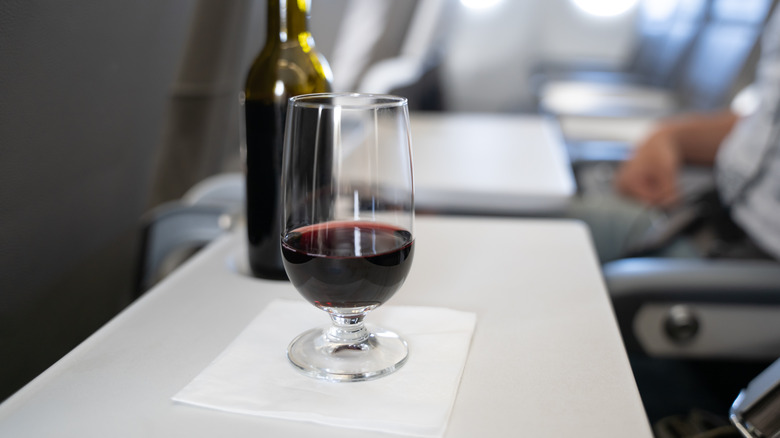 A glass with red wine and a small bottle in the background on the table of a passenger in an airplane.