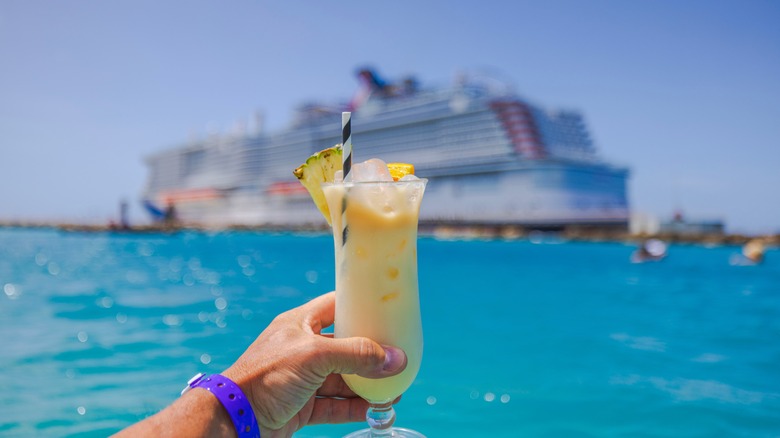 Hand holding a cocktail in front of a cruise ship