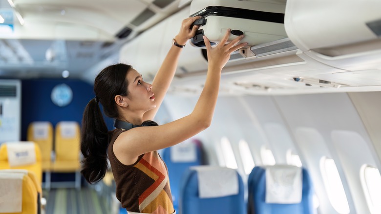 Traveler stows their carry-on luggage in an overhead bin