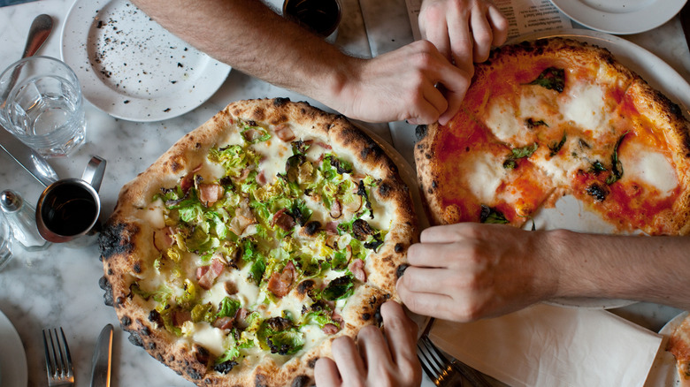 Hands reaching for slices of two pizzas at the dinner tables