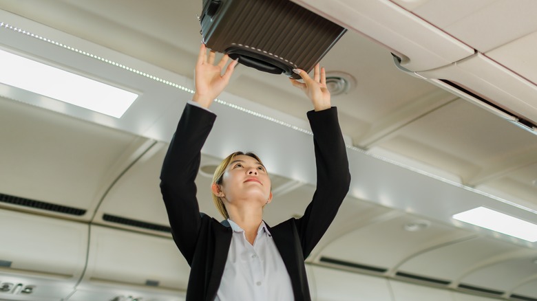 Traveler pulling luggage down from an overhead compartment