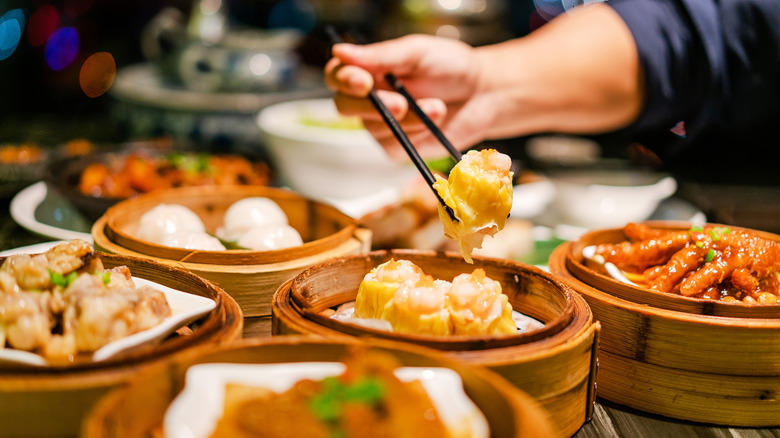 Close-up of a hand holding chopsticks over bamboo baskets of dim sum
