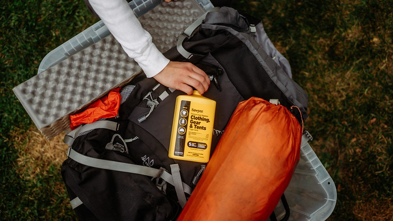 Bottle of Sawyer Products Permethrin Insect Spray being put into a backpack with camping gear