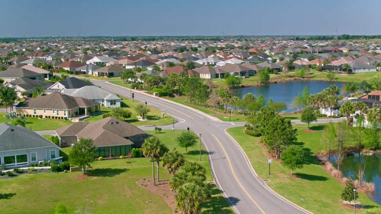 An aerial shot of single-story homes surrounded by trees, lawns, and a lake in The Villages community in Florida
