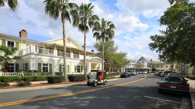 A man driving a golf cart past palm trees and a white villa in The Villages, a retirement community in Florida